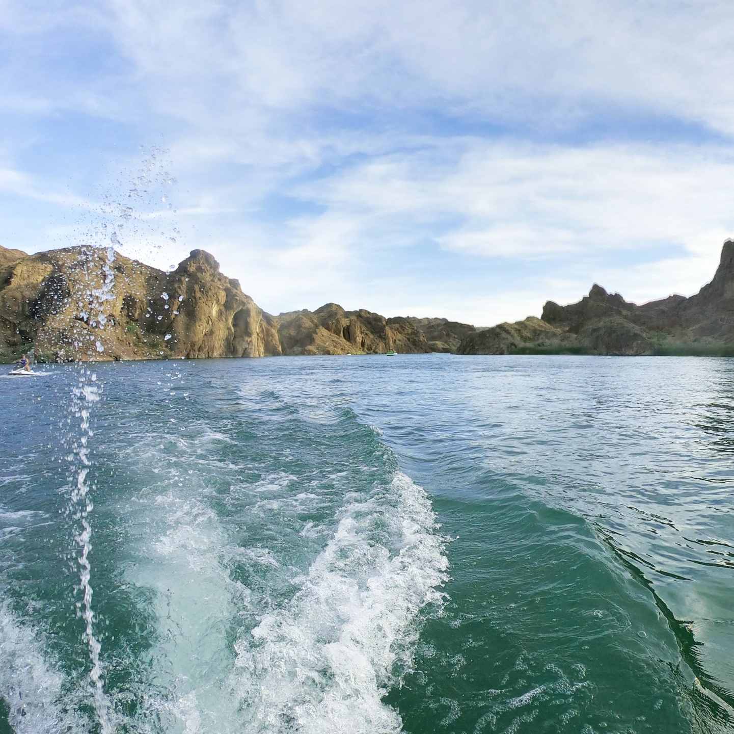 Jet ski spray on a lake below rocky hills